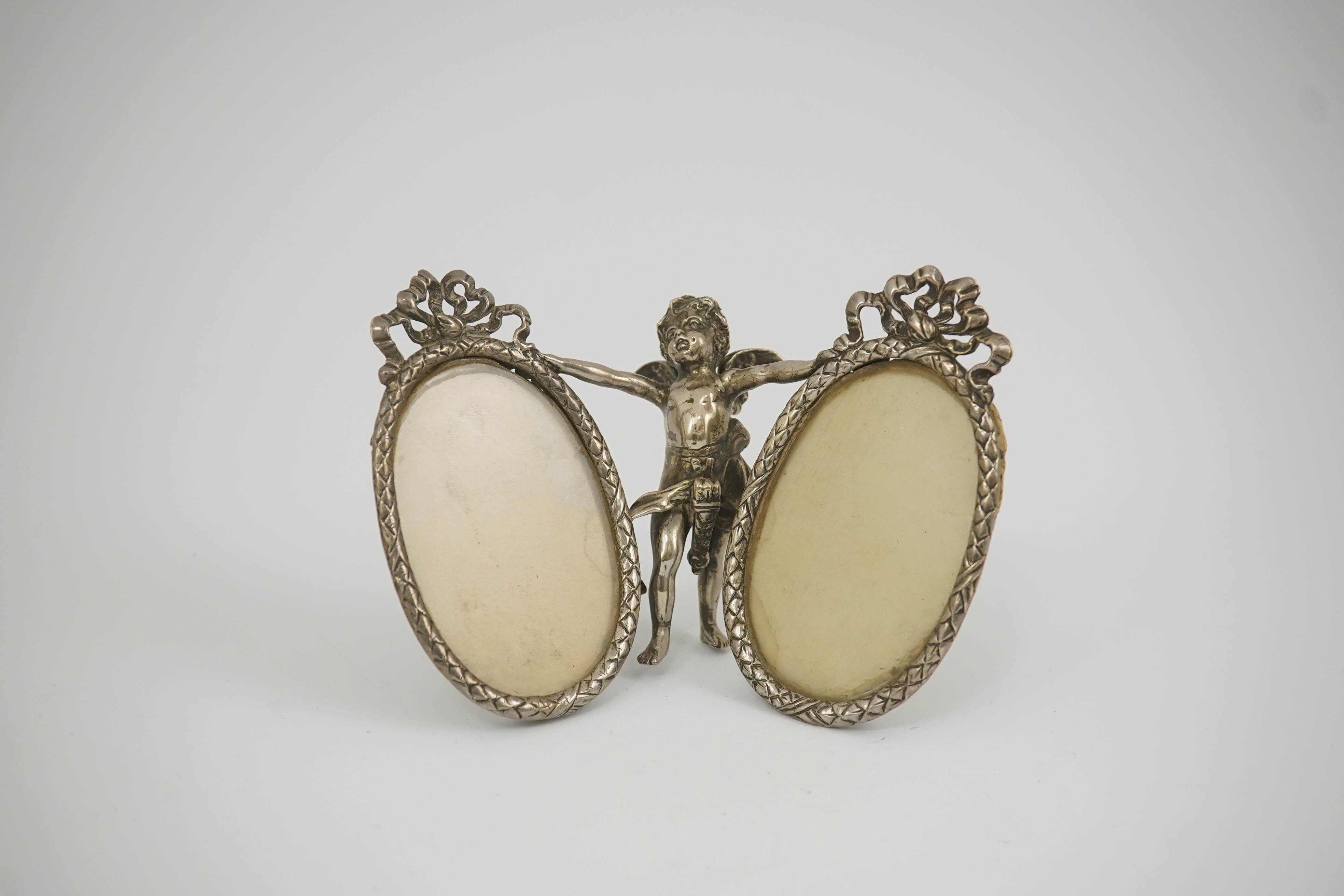 A late 19th century Hanau silver double oval photograph frame, supported by central figure of Cupid, by Berthold Muller